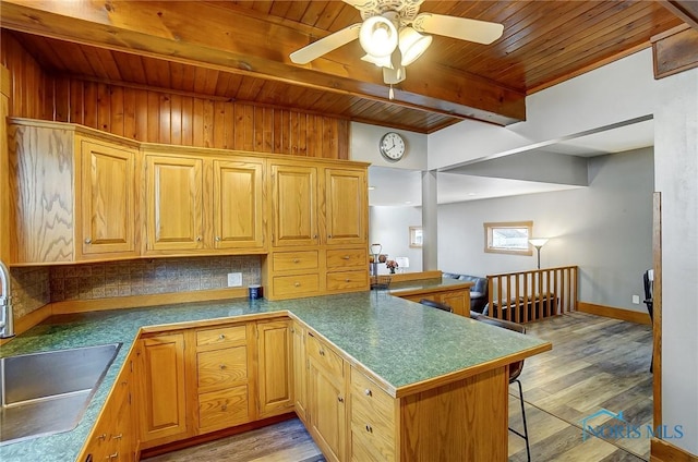 kitchen with light wood finished floors, dark countertops, a peninsula, a sink, and beam ceiling