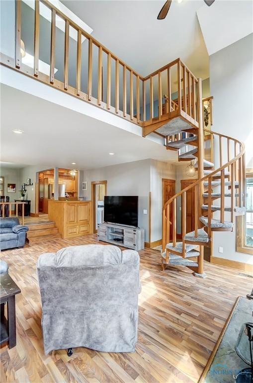 living room featuring light wood finished floors, a towering ceiling, a ceiling fan, baseboards, and stairs