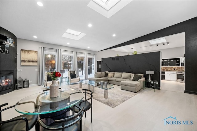 living room featuring a skylight, a fireplace, light wood-style flooring, and recessed lighting