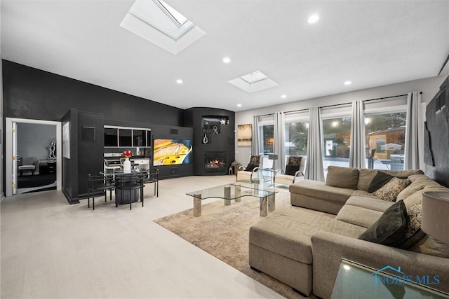 living room featuring light wood-type flooring, recessed lighting, a warm lit fireplace, and vaulted ceiling with skylight