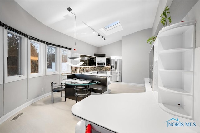 interior space featuring vaulted ceiling with skylight, stainless steel appliances, visible vents, light countertops, and backsplash