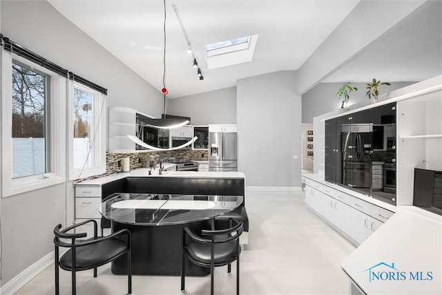 kitchen featuring vaulted ceiling with skylight, freestanding refrigerator, light countertops, white cabinetry, and stainless steel refrigerator with ice dispenser