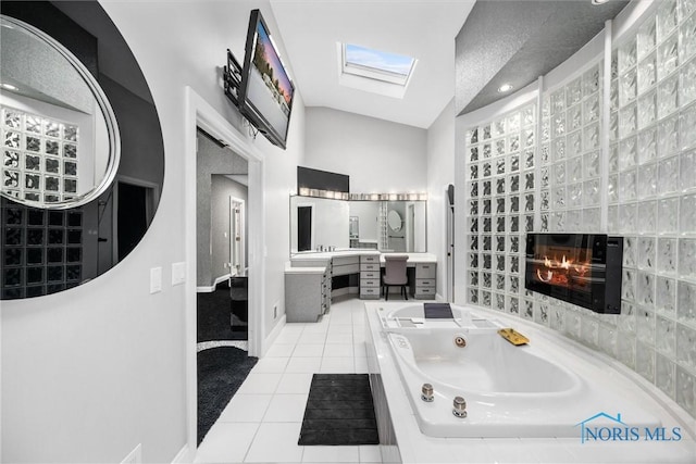 full bathroom featuring vaulted ceiling with skylight, vanity, tile patterned floors, a whirlpool tub, and a glass covered fireplace