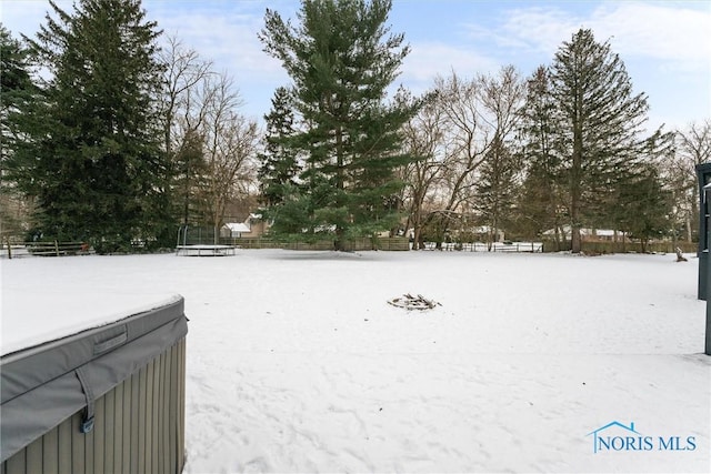 yard covered in snow featuring a trampoline and fence