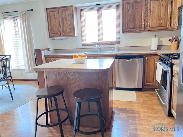 kitchen featuring light wood-style flooring, a kitchen island, stainless steel appliances, light countertops, and a sink