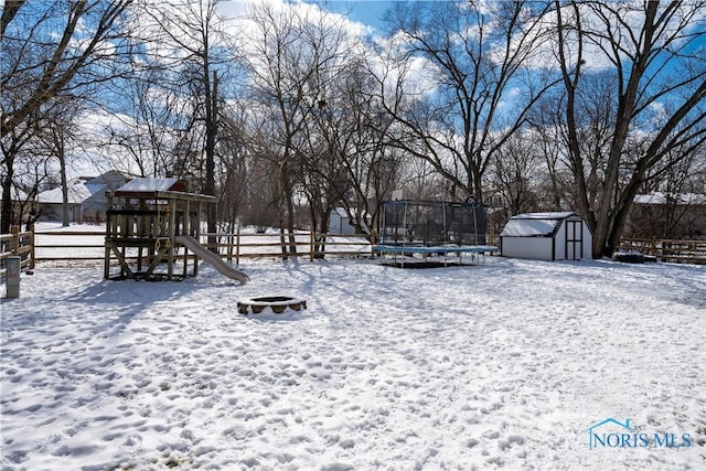 yard covered in snow with a playground, a fire pit, a storage shed, fence, and a trampoline