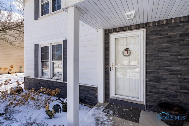 snow covered property entrance with stone siding