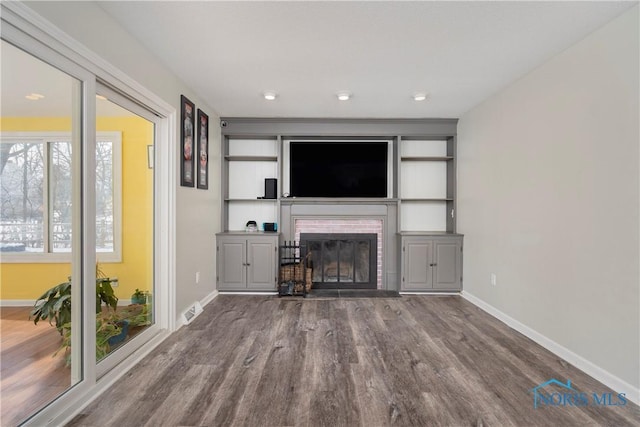 unfurnished living room featuring a brick fireplace, visible vents, baseboards, and wood finished floors