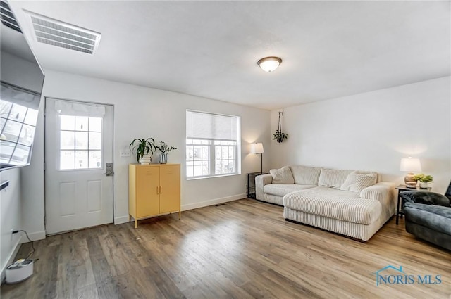 living room featuring a wealth of natural light, visible vents, baseboards, and wood finished floors