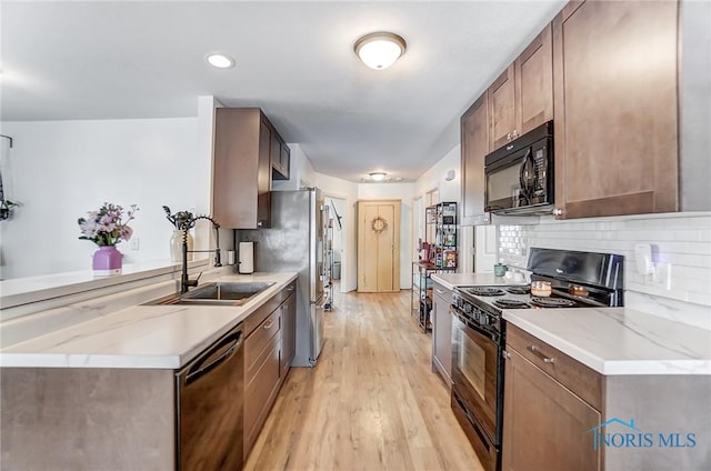 kitchen with black appliances, light wood finished floors, backsplash, and a sink