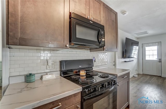 kitchen with light stone counters, tasteful backsplash, visible vents, wood finished floors, and black appliances