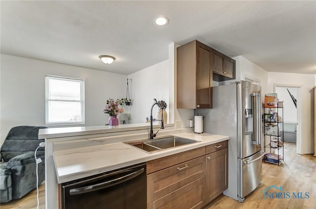 kitchen with light wood finished floors, light countertops, a sink, dishwasher, and stainless steel fridge with ice dispenser