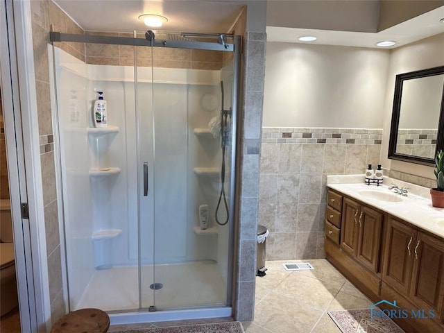 full bath featuring tile walls, visible vents, toilet, a shower stall, and vanity