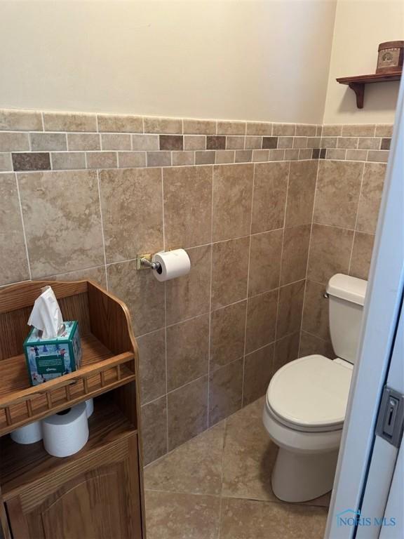 bathroom with a wainscoted wall, tile walls, toilet, and tile patterned floors