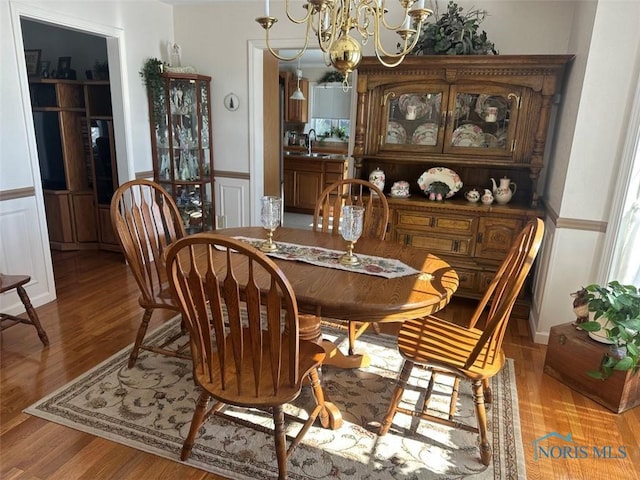 dining space with light wood-style floors, a wainscoted wall, a notable chandelier, and a decorative wall