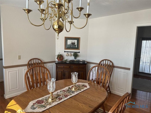 dining room featuring dark wood-type flooring, a decorative wall, wainscoting, and an inviting chandelier