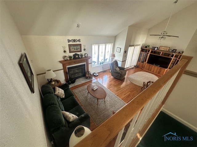 living area with a fireplace with flush hearth, vaulted ceiling, baseboards, and wood finished floors