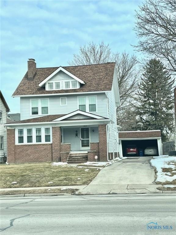 traditional style home featuring a garage, a chimney, an outbuilding, covered porch, and brick siding