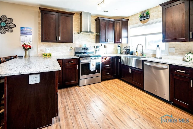 kitchen with appliances with stainless steel finishes, light wood-type flooring, wall chimney range hood, and a peninsula