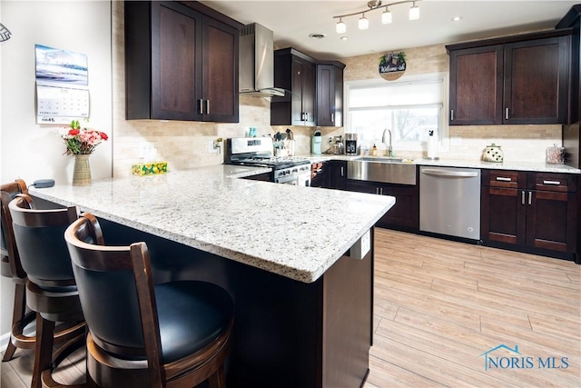 kitchen with stainless steel appliances, a breakfast bar, a peninsula, and wall chimney exhaust hood