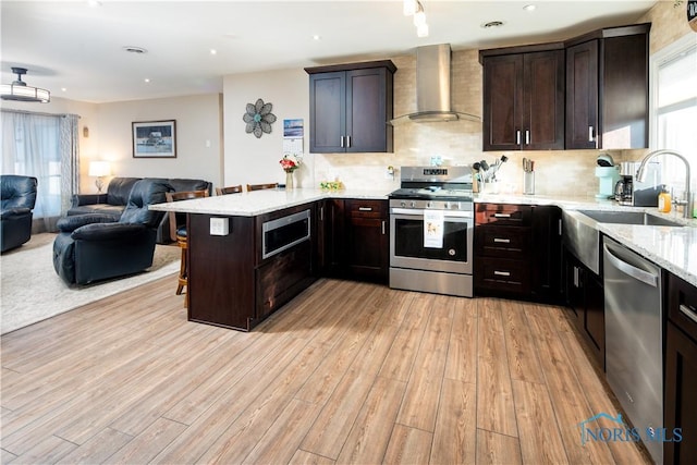 kitchen featuring a breakfast bar, stainless steel appliances, open floor plan, a peninsula, and wall chimney exhaust hood