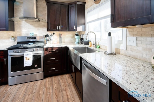 kitchen with appliances with stainless steel finishes, light wood-style floors, wall chimney range hood, and light stone counters