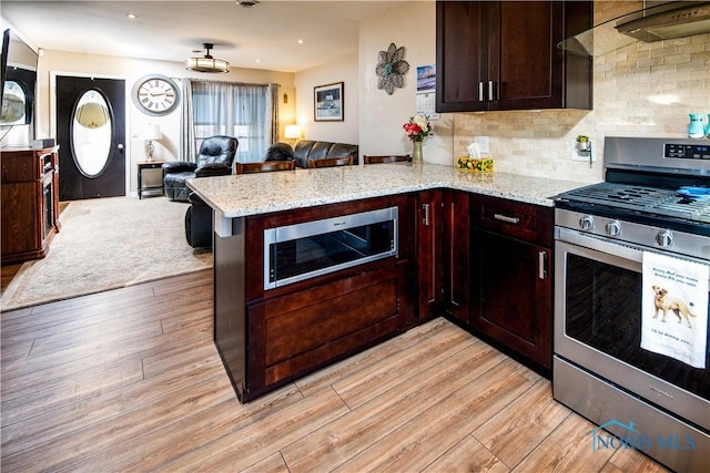 kitchen featuring light stone counters, appliances with stainless steel finishes, open floor plan, light wood-type flooring, and a peninsula