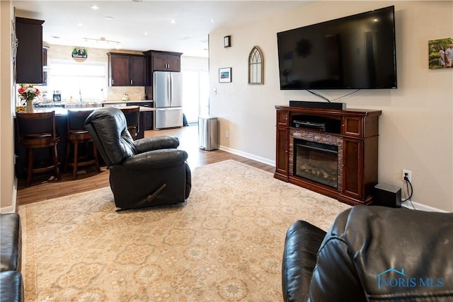 living area with light wood-style floors, baseboards, and a glass covered fireplace