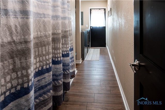 corridor featuring a textured wall, dark wood-style flooring, washer and clothes dryer, and baseboards