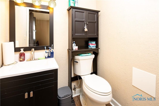 bathroom with toilet, a textured wall, vanity, and baseboards