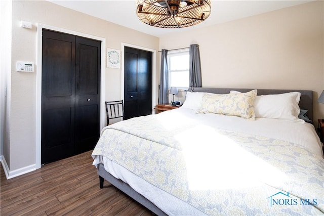 bedroom with multiple closets, baseboards, and dark wood-style flooring