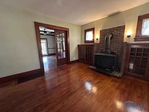 unfurnished living room featuring dark wood-style floors, a wood stove, french doors, and baseboards