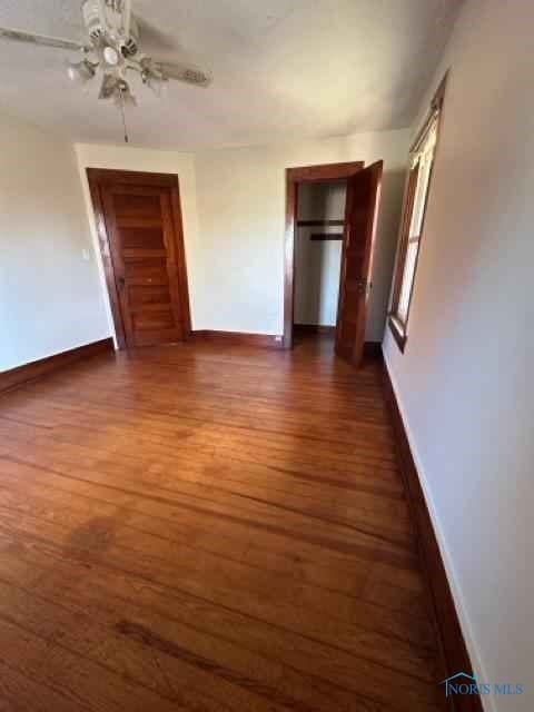 interior space featuring a ceiling fan, baseboards, and dark wood-type flooring