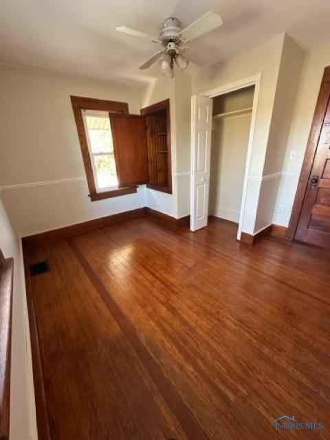 unfurnished bedroom with a ceiling fan, a closet, baseboards, and dark wood-type flooring