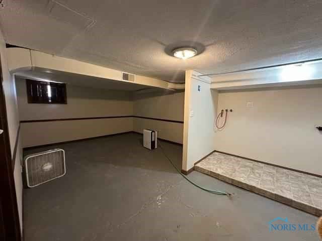 finished below grade area featuring visible vents, a textured ceiling, and baseboards