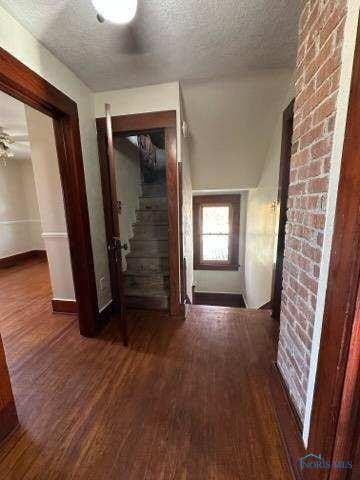 hall featuring a textured ceiling, dark wood-type flooring, stairs, and baseboards