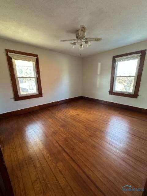 unfurnished room with dark wood-type flooring, a healthy amount of sunlight, a textured ceiling, and baseboards