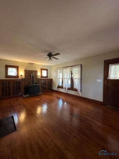 unfurnished living room with a wood stove, ceiling fan, baseboards, and wood finished floors