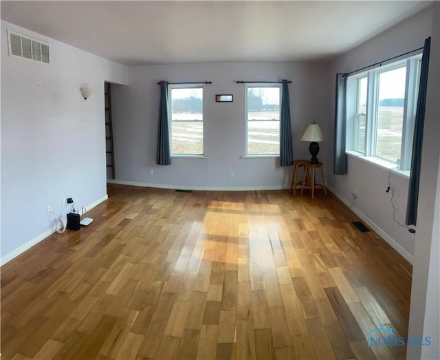 spare room with light wood finished floors, visible vents, and baseboards