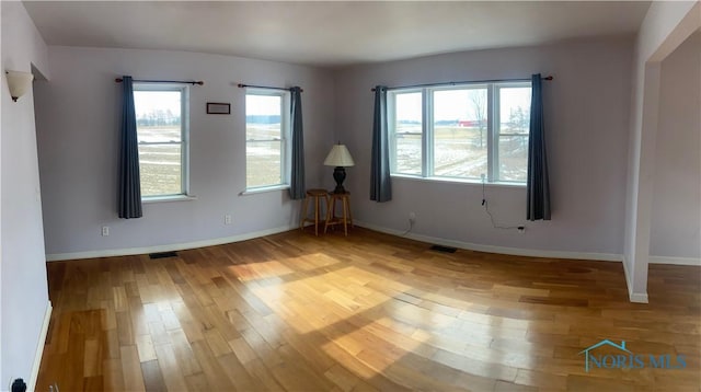 empty room with wood finished floors, visible vents, and baseboards