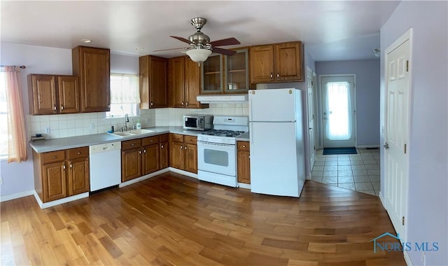 kitchen featuring light countertops, decorative backsplash, brown cabinetry, a sink, and white appliances