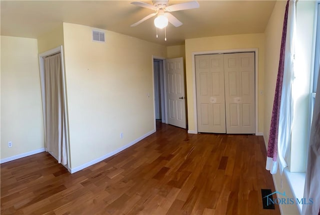 unfurnished bedroom with baseboards, visible vents, ceiling fan, dark wood-type flooring, and a closet