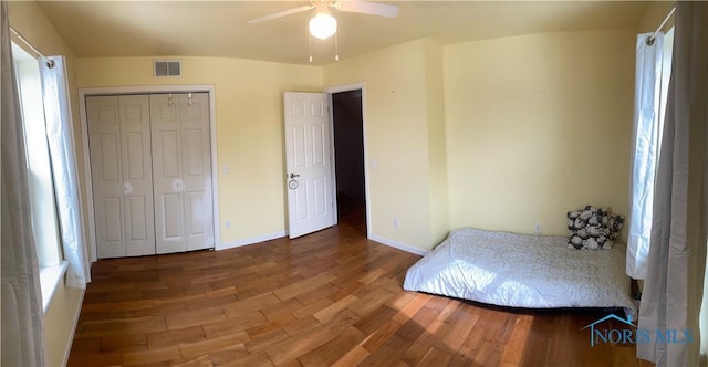 bedroom with a closet, visible vents, ceiling fan, wood finished floors, and baseboards