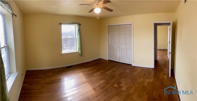 unfurnished bedroom featuring visible vents, baseboards, ceiling fan, dark wood-type flooring, and a closet