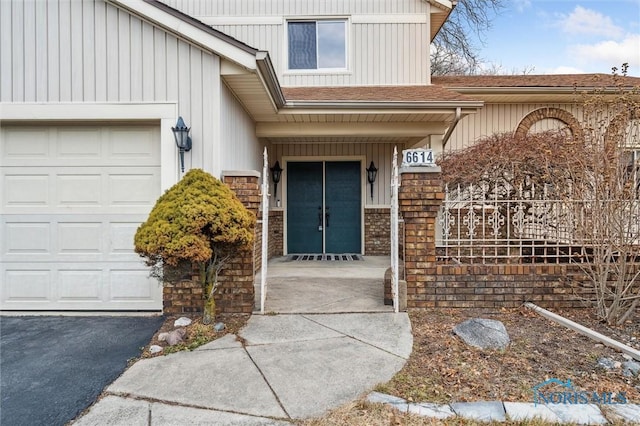 doorway to property with an attached garage, roof with shingles, aphalt driveway, and brick siding