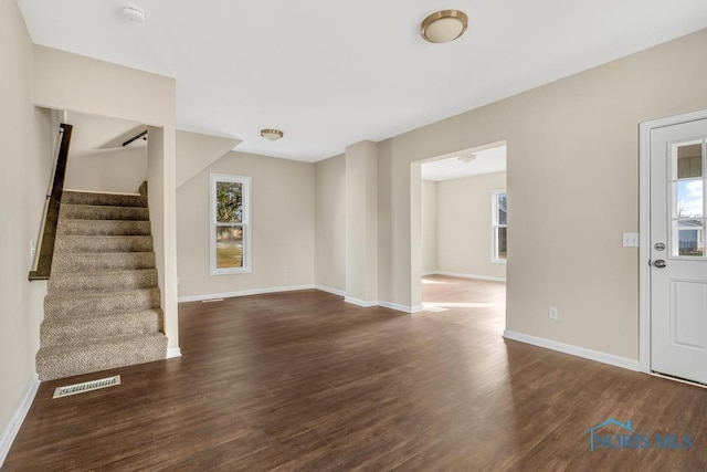 unfurnished living room with dark wood-style floors, a wealth of natural light, stairs, and visible vents