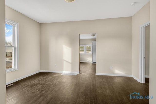 unfurnished room with plenty of natural light, visible vents, baseboards, and dark wood-style flooring