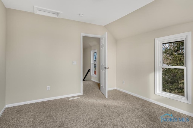 carpeted spare room featuring vaulted ceiling and baseboards