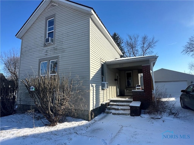 view of snowy exterior with covered porch, an outbuilding, and cooling unit