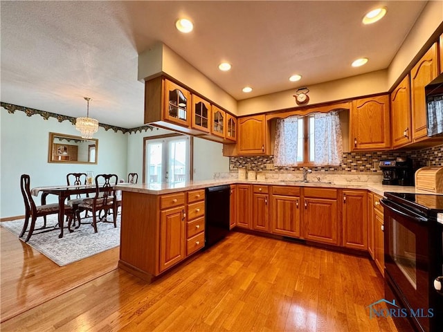 kitchen with a peninsula, black appliances, glass insert cabinets, and light countertops